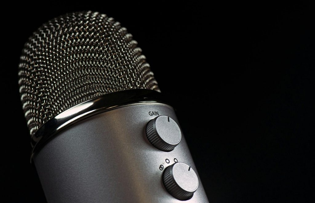 Detailed close-up of a silver mesh microphone with gain control knobs against a dark background.